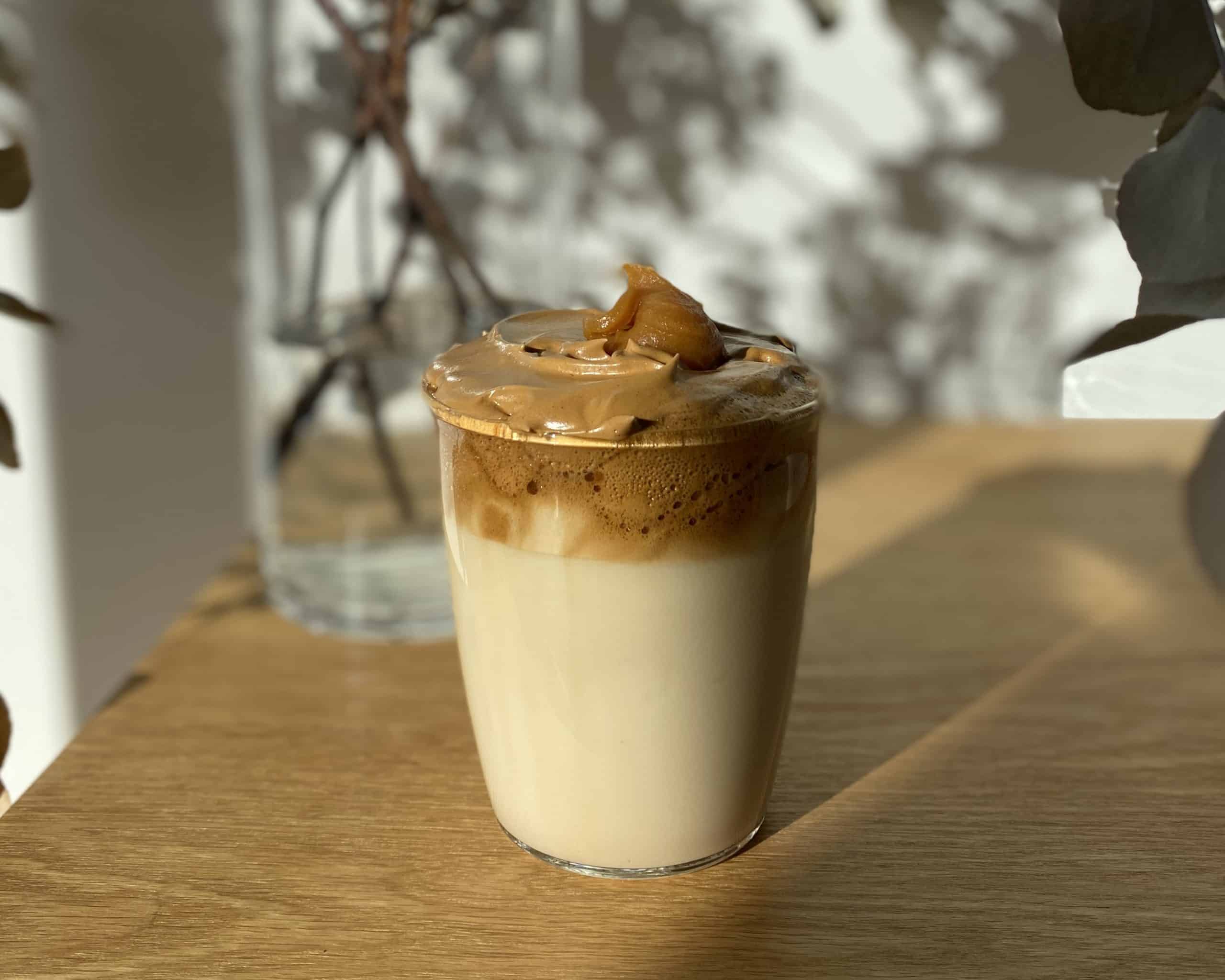 Glass tumbler filled with milk, topped with Dirty Chai Dalgona