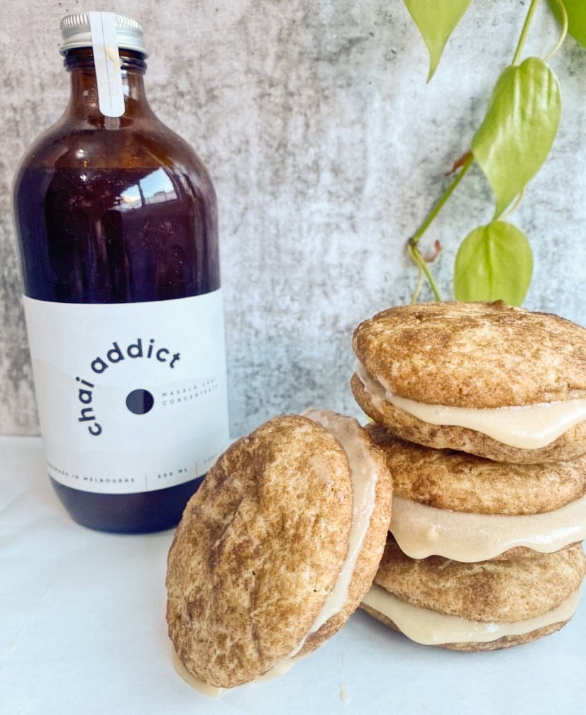 four Chai Addict Cookie Sandwiches next to a bottle of chai concentrate