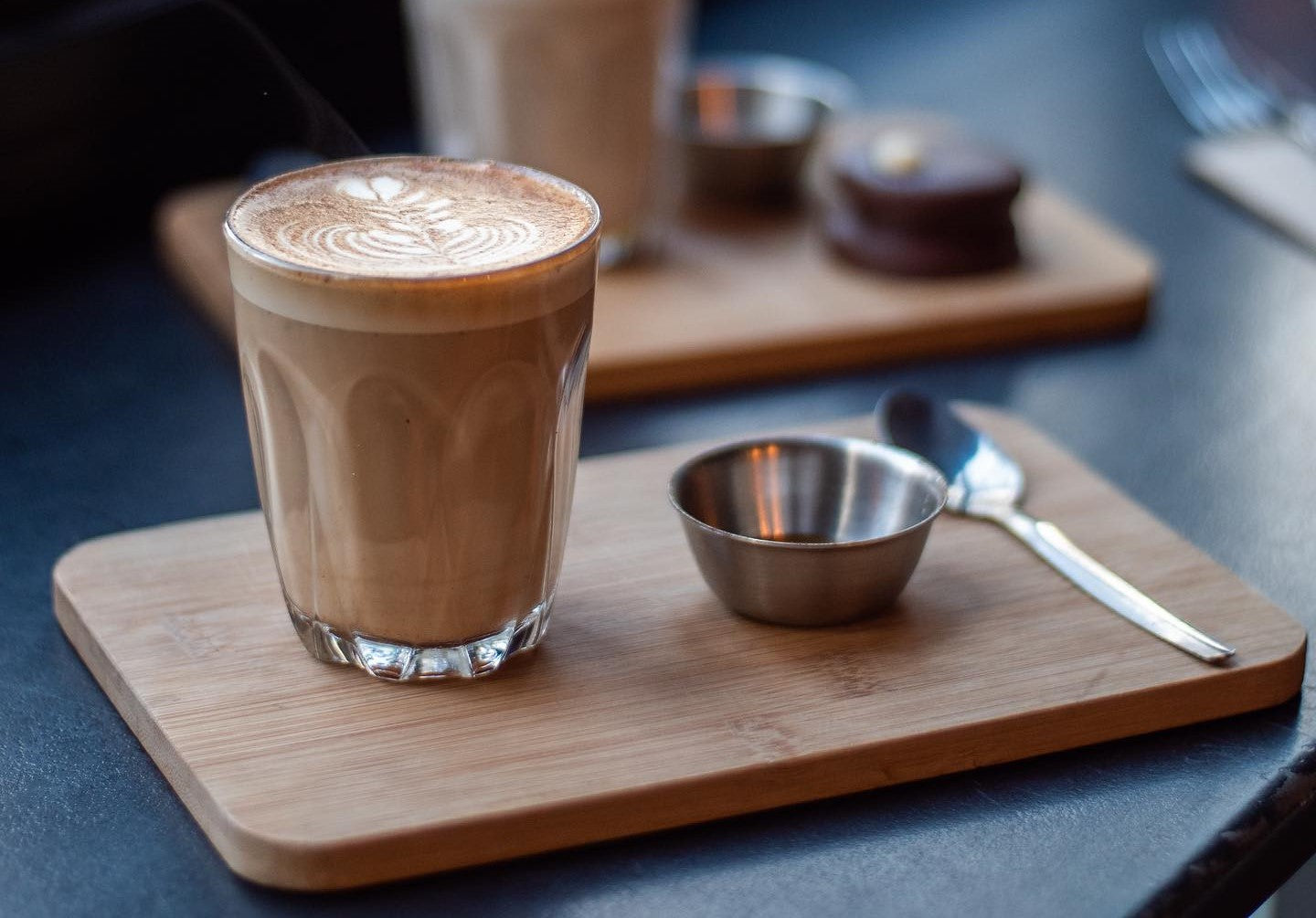 an enticing cup of dirty chai latte sits on a wooden board with a small saucer of honey and teaspoon