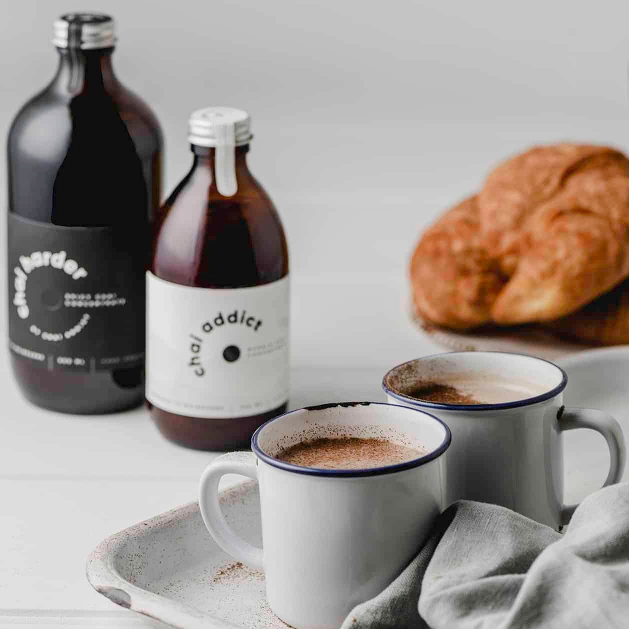 Steaming cup of aromatic chai latte served in a ceramic mug, garnished with cinnamon sticks and star anise, resting on a rustic white metal tray