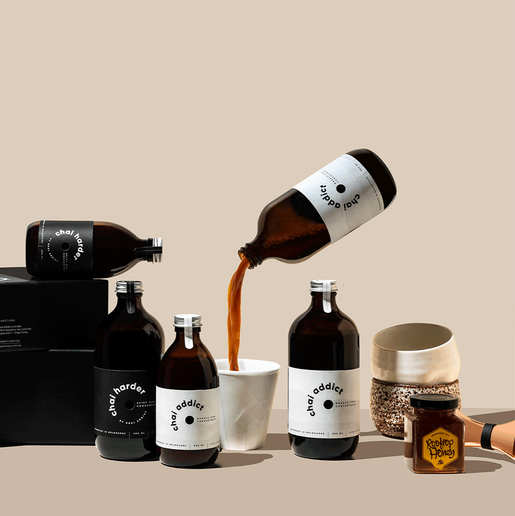 enticing chai imagery with gift boxes, chai concentrate bottles, cups, honey, jigger and a floating chai addict pouring chai concentrate liquid to a white ceramic cup ideal for sharing the joy of chai latte with loved ones