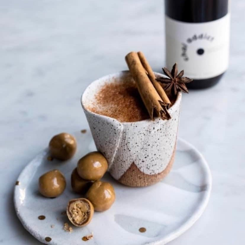 Inviting display of chai latte topped with cinnamon and side of chocolate balls, a bottle of chai addict masala chai vibrant packaging, showcasing the rich variety of flavours and aromas