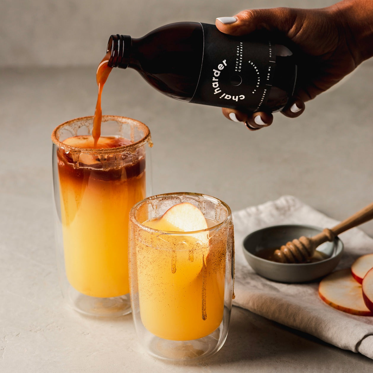 person pouring chai harder spicy chai concentrate to a glass tumbler filled with apple juice to create a delicious recipe for refreshing chai soda