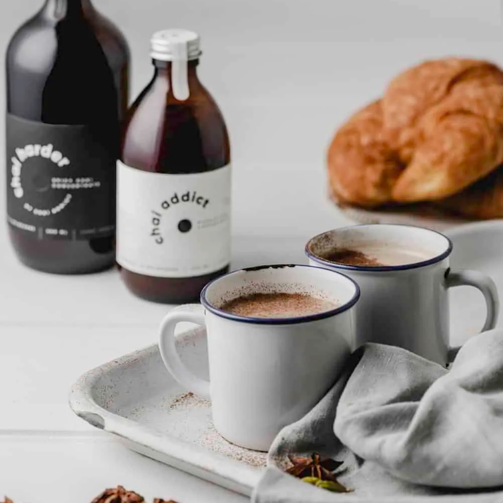Steaming cup of aromatic chai latte served in a ceramic mug, garnished with cinnamon sticks and star anise, resting on a rustic white metal tray