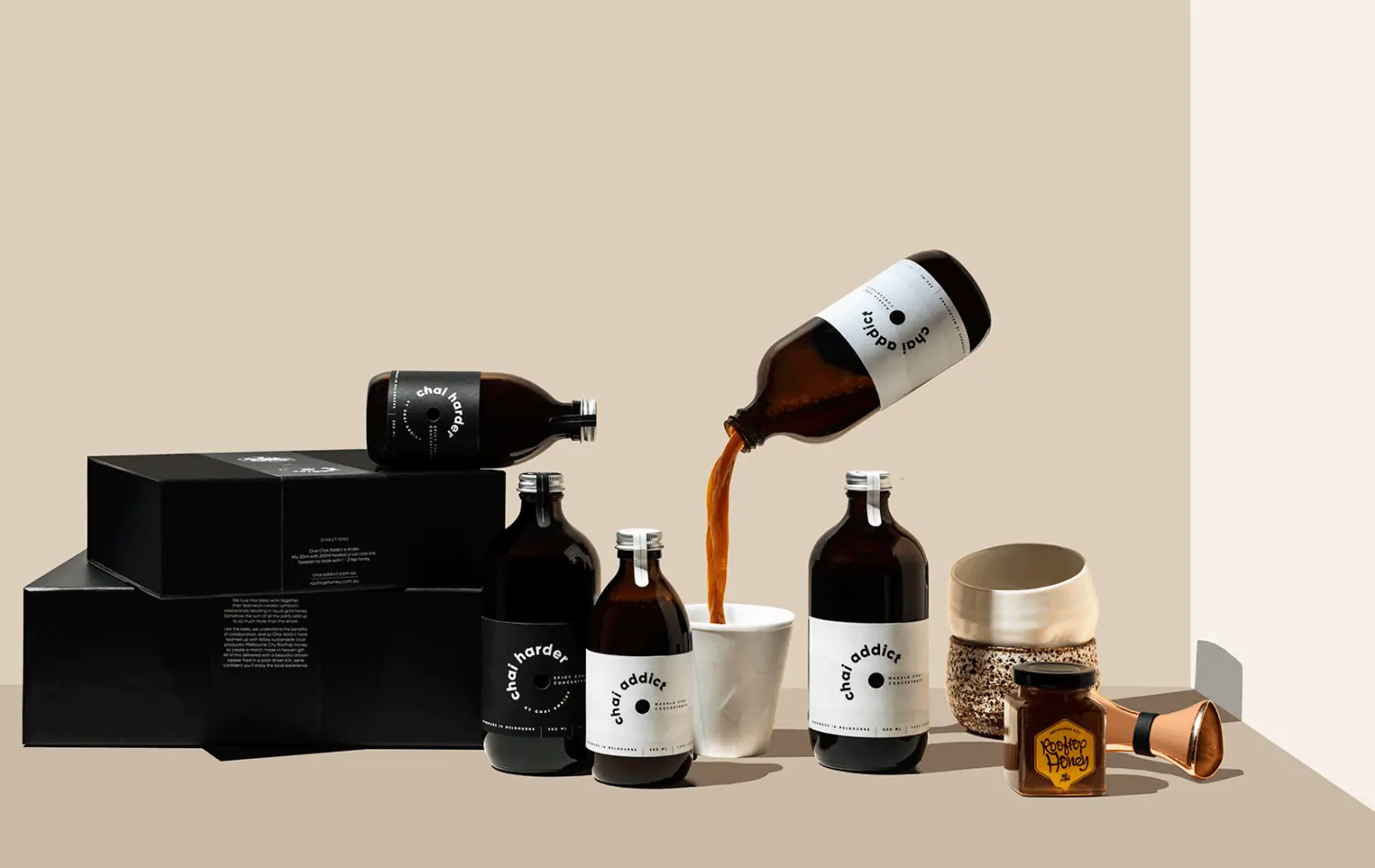 enticing chai imagery with gift boxes, chai concentrate bottles, cups, honey, jigger and a floating chai addict pouring chai concentrate liquid to a white ceramic cup ideal for sharing the joy of chai latte with loved ones