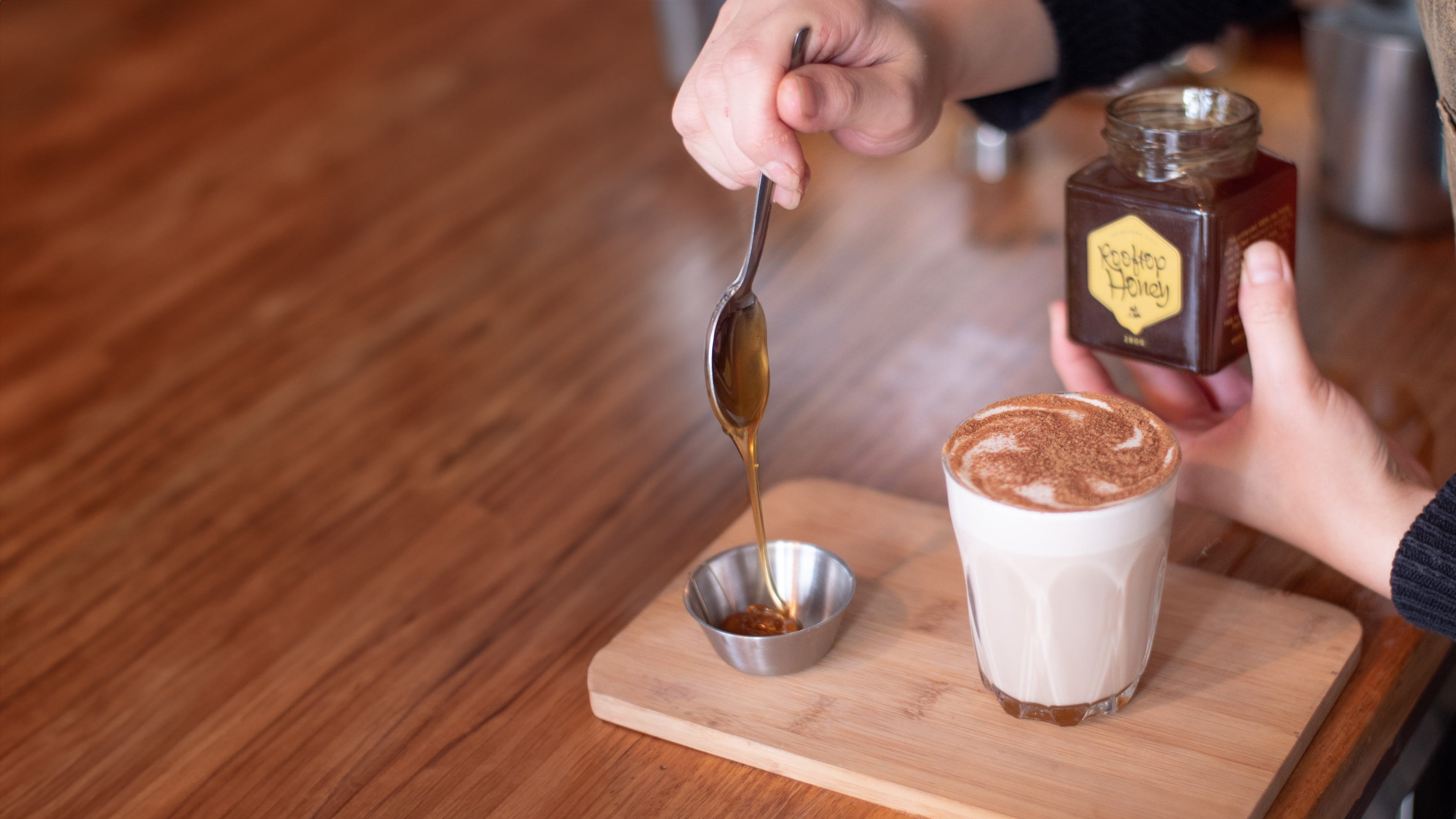 Barista drizzling honey to a small saucer, that will be used to mix with a steaming cup of aromatic chai latte