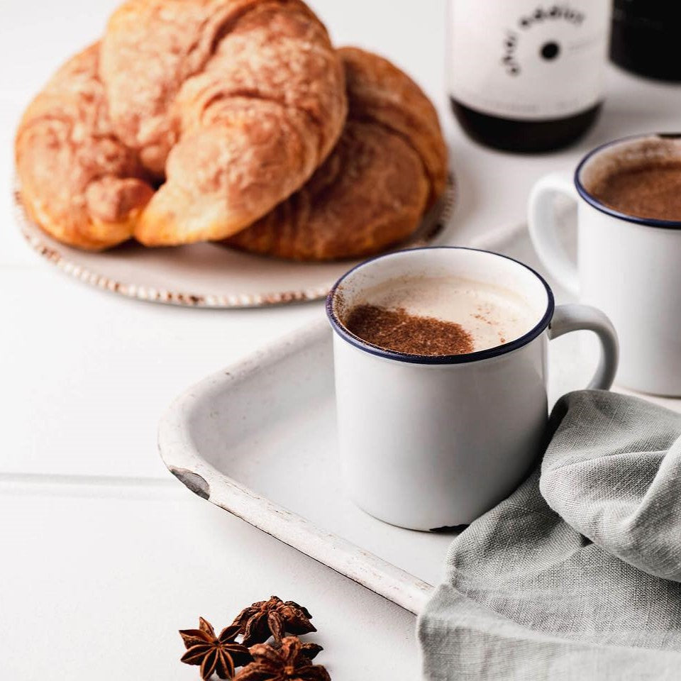 Steaming cup of aromatic chai latte served in a ceramic mug, garnished with cinnamon sticks and star anise, resting on a rustic white metal tray