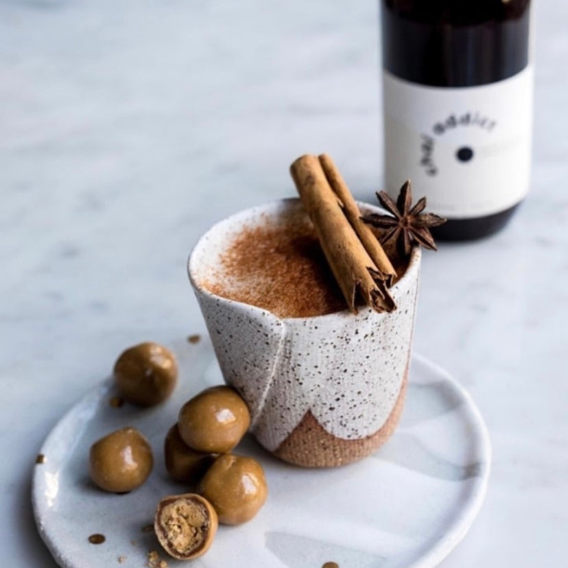Inviting display of chai latte topped with cinnamon and side of chocolate balls, a bottle of chai addict masala chai vibrant packaging, showcasing the rich variety of flavours and aromas