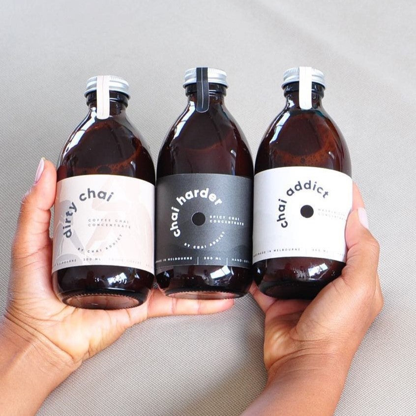 a selection of three chai addict chai concentrates bottles held in between a person's hand