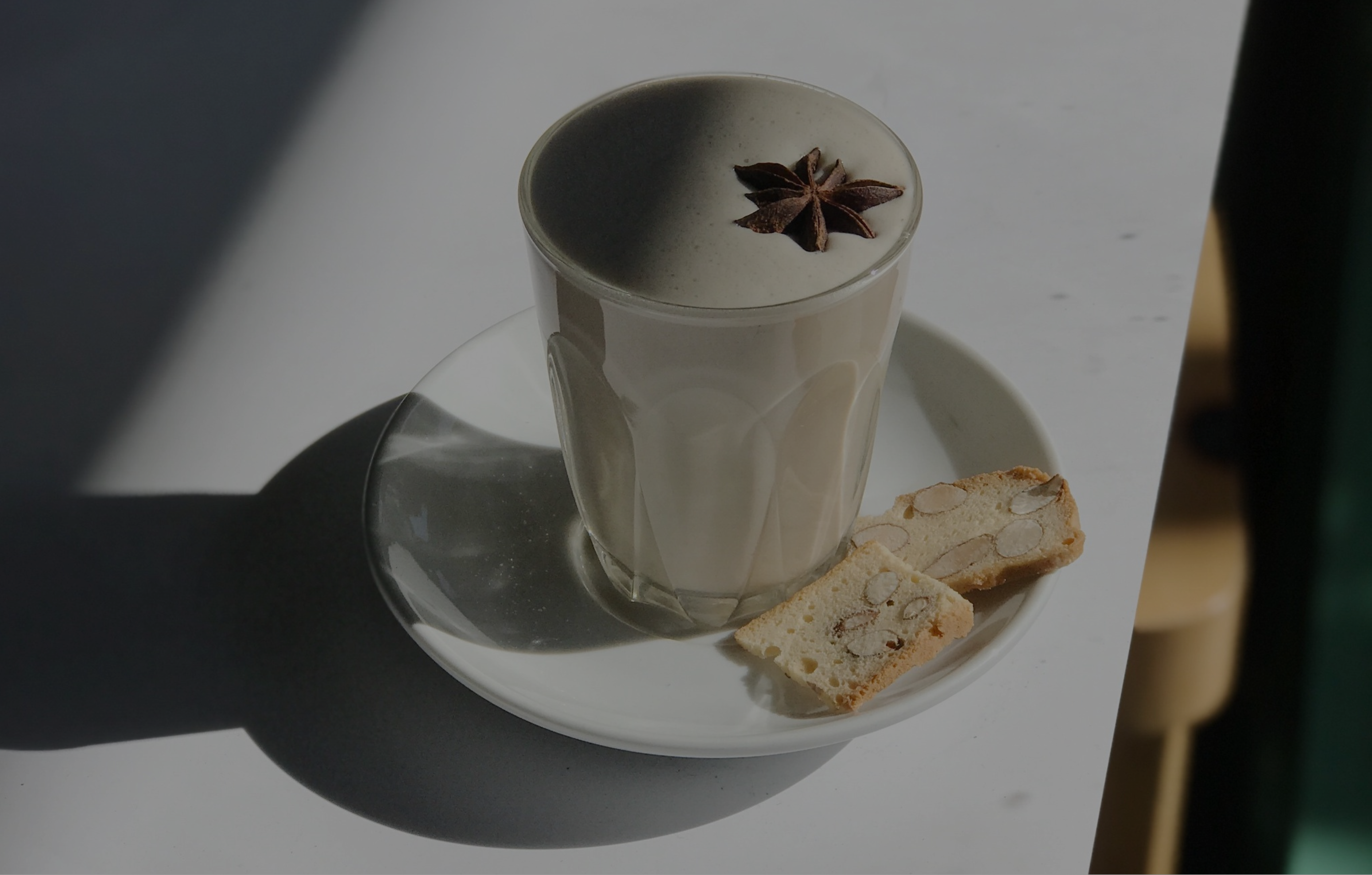 A cup of chai latte garnished with star anise, served on top of a side plate with biscotti, infusing the air with anticipation and delight