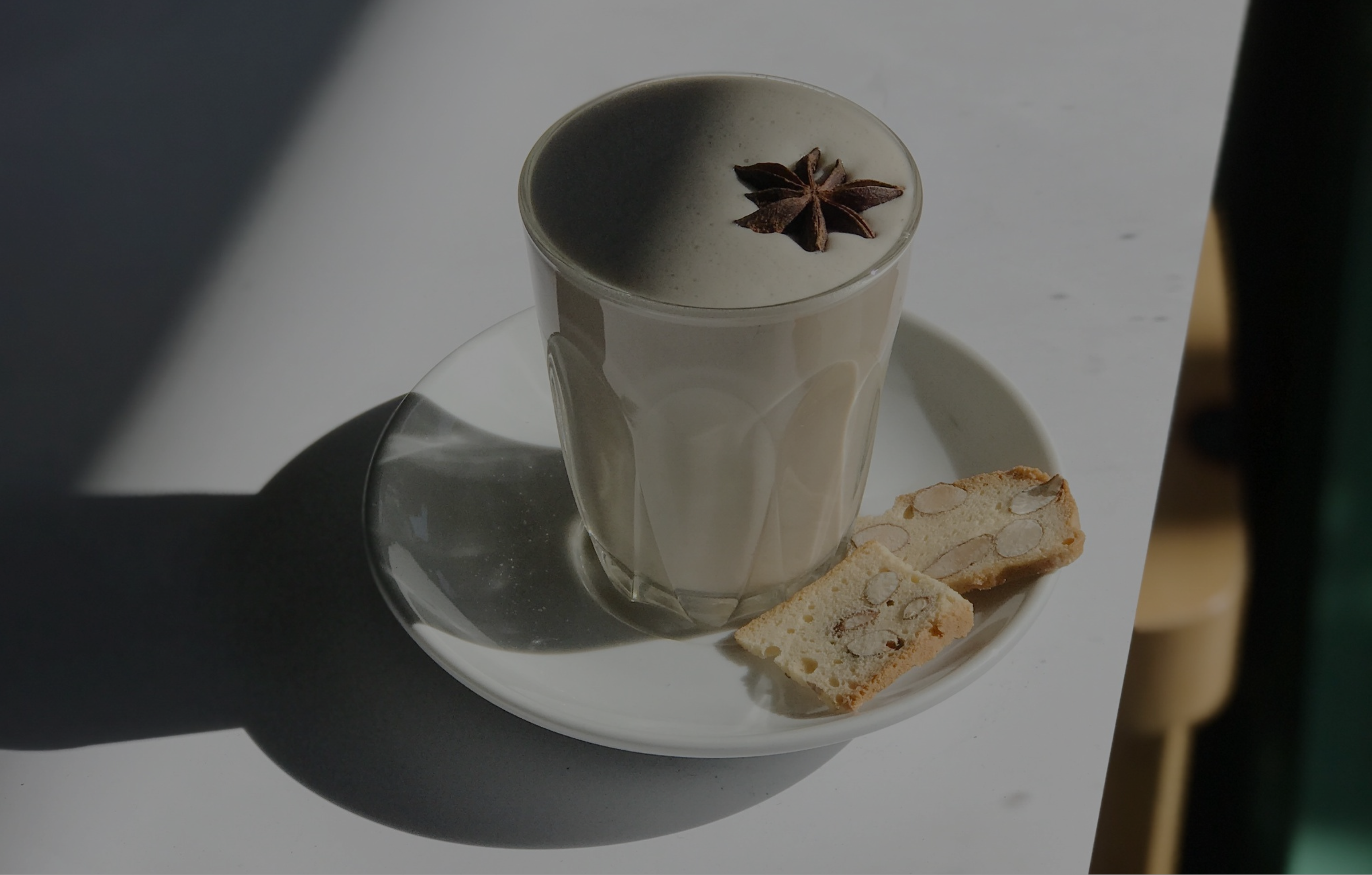  A cup of chai latte garnished with star anise, served on top of a side plate with biscotti, infusing the air with anticipation and delight