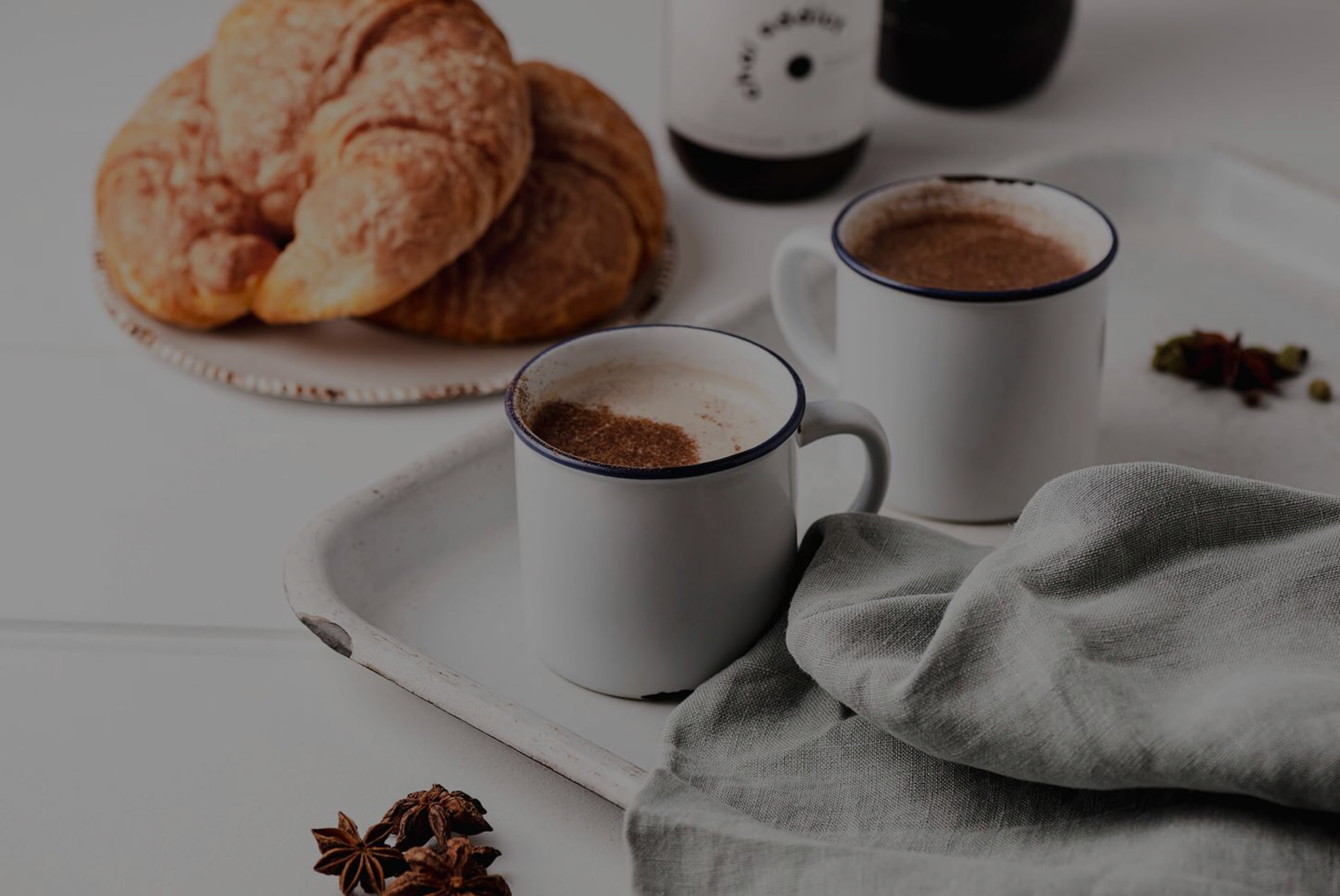 Two mugs of steaming chai latte served with a side of croissants, the epitome of chai perfection promising a sensory journey of aromatic bliss