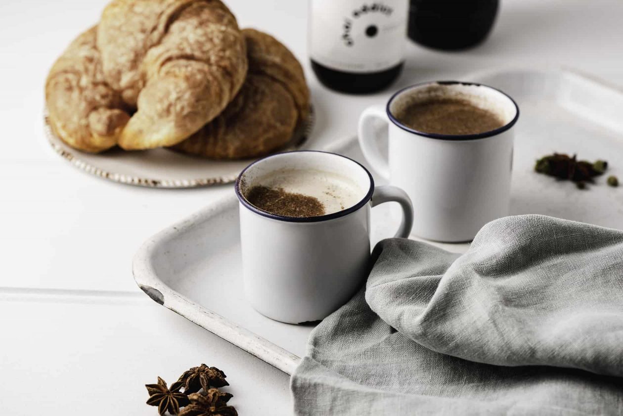 Steaming cup of aromatic chai latte served in a ceramic mug, garnished with cinnamon sticks and star anise, resting on a rustic white metal tray