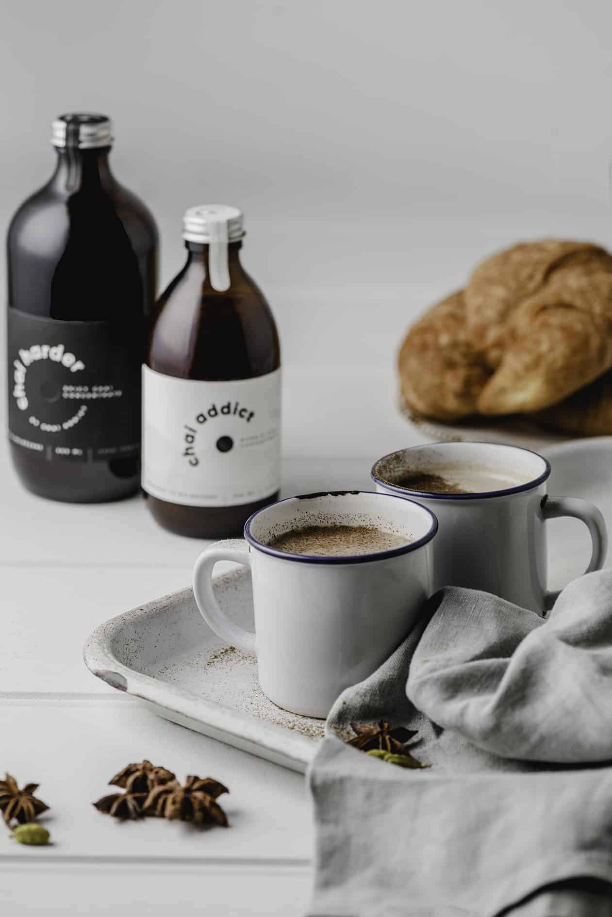 Steaming cup of aromatic chai latte served in a ceramic mug, garnished with cinnamon sticks and star anise, resting on a rustic white metal tray
