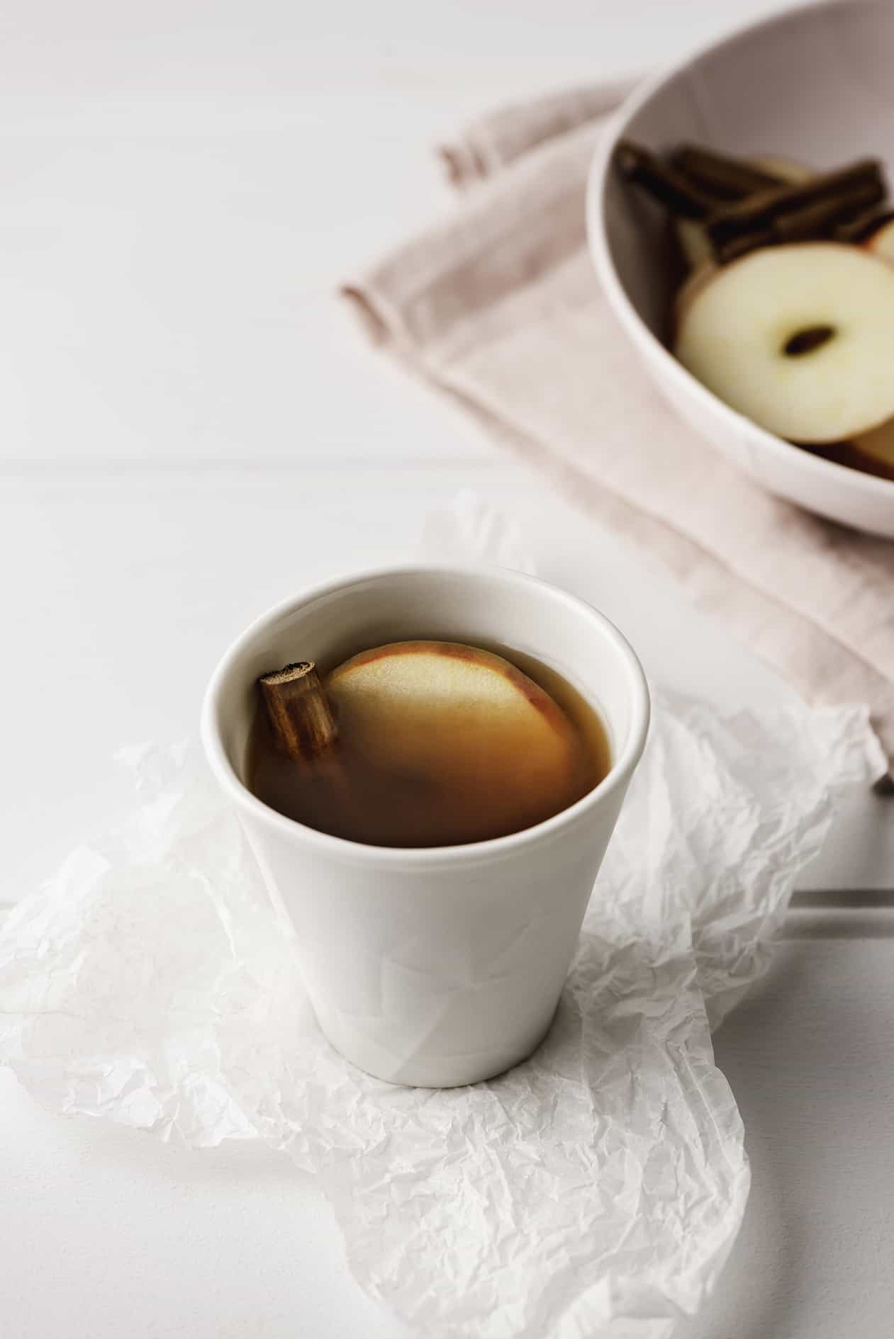 enticing cup of hot chai tea served with round slice of apple and cinnamon in a white ceramic cup