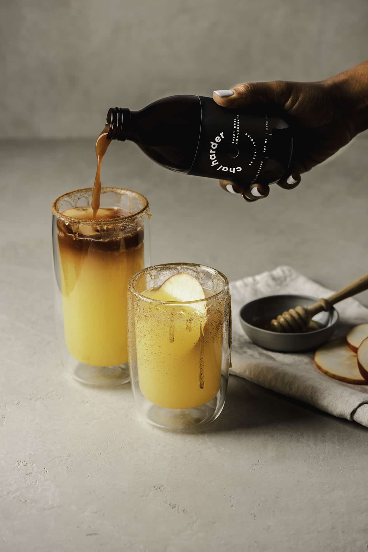 person pouring chai harder spicy chai concentrate to a glass tumbler filled with apple juice to create a delicious recipe for refreshing chai soda