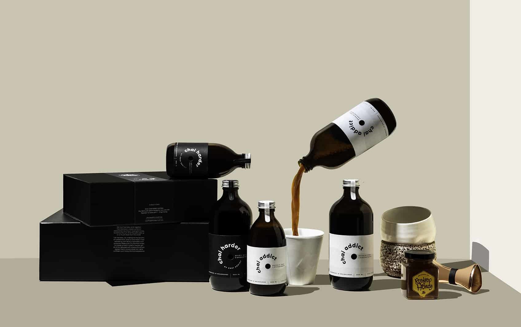 enticing chai imagery with gift boxes, chai concentrate bottles, cups, honey, jigger and a floating chai addict pouring chai concentrate liquid to a white ceramic cup ideal for sharing the joy of chai latte with loved ones