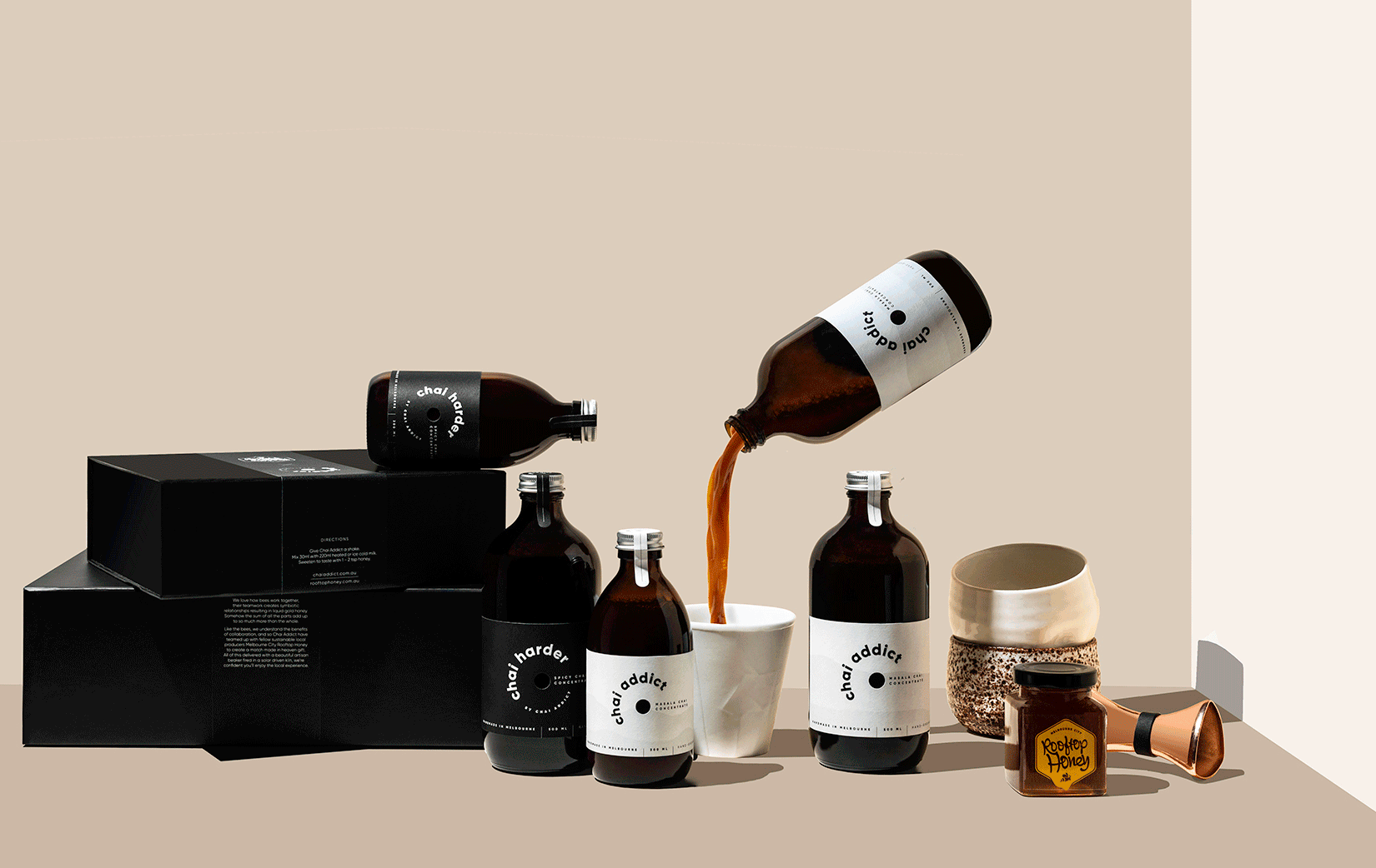 enticing chai imagery with gift boxes, chai concentrate bottles, cups, honey, jigger and a floating chai addict pouring chai concentrate liquid to a white ceramic cup ideal for sharing the joy of chai latte with loved ones