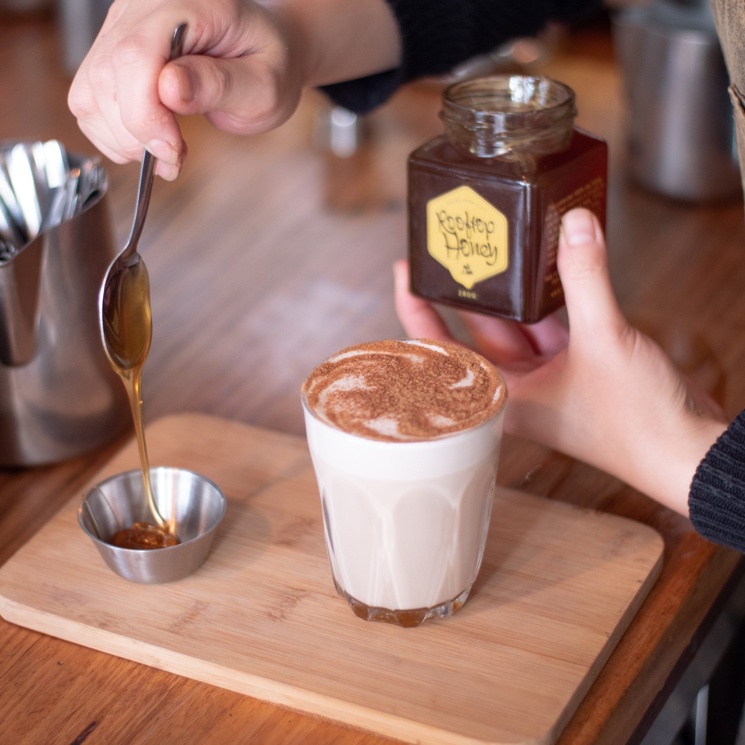 Barista drizzling honey to a small saucer, that will be used to mix with a steaming cup of aromatic chai latte