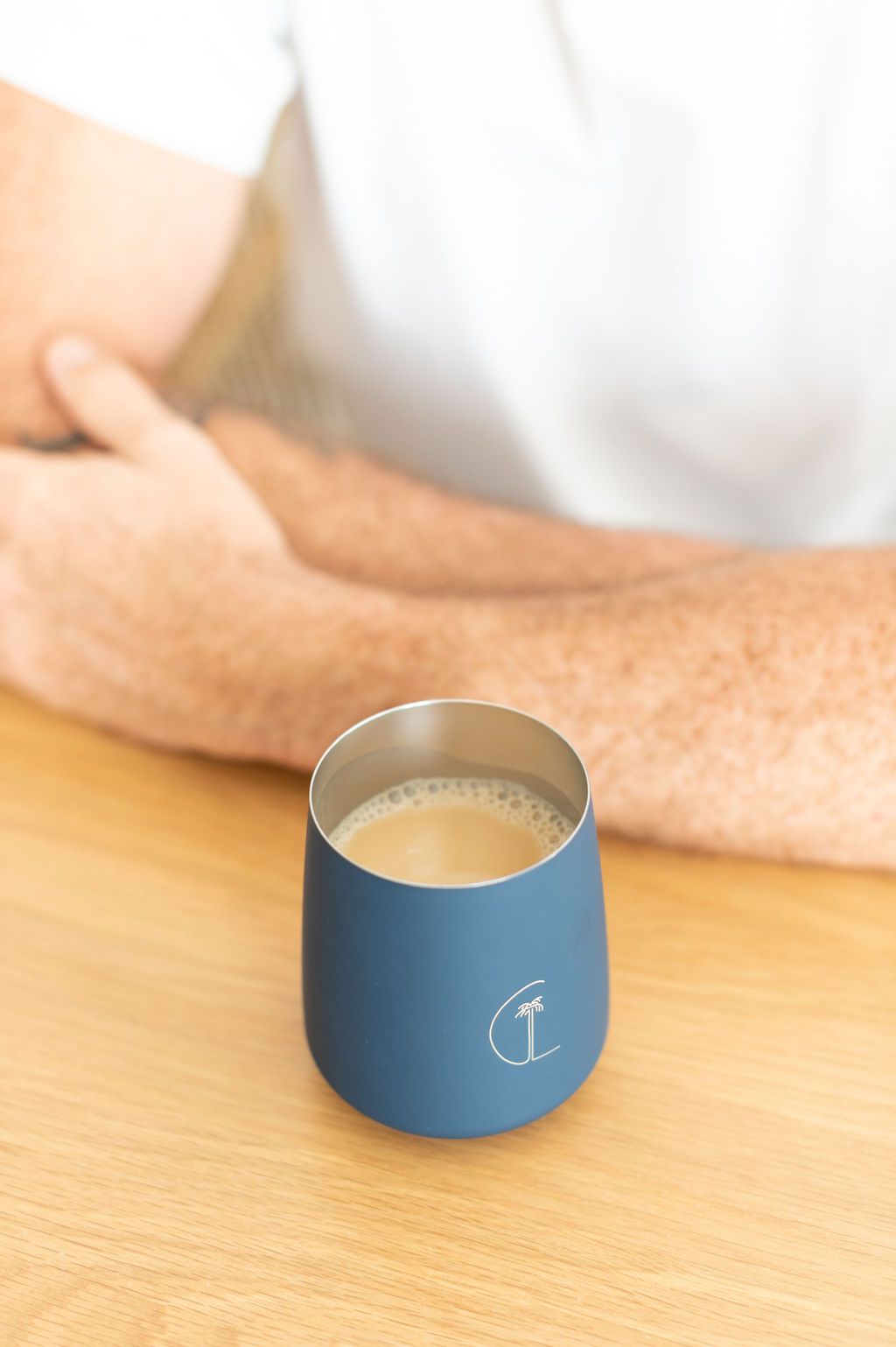 man sitting behind caye life navy keep cup filled with chai latte