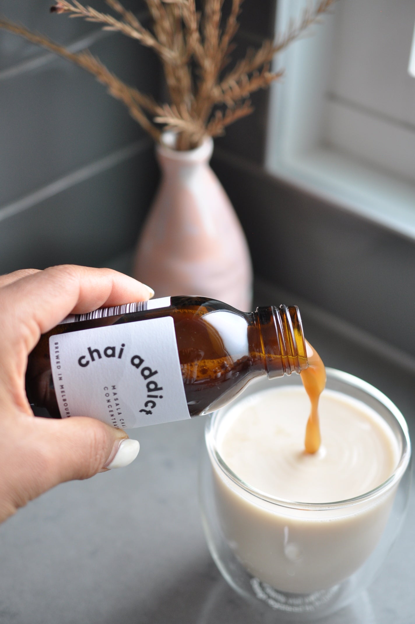 person pouring liquid chai tea concentrate to a cup of plant milk