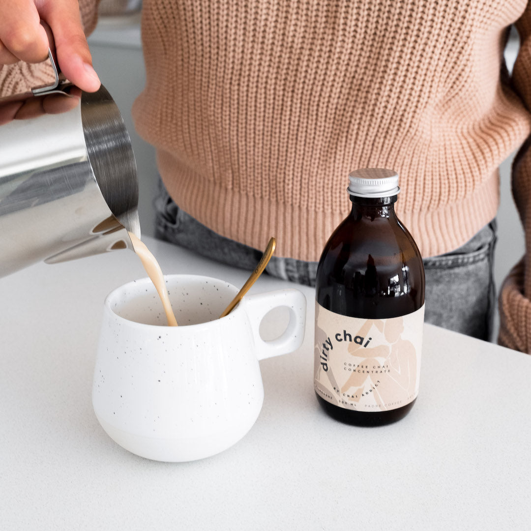 Person pouring dirty chai latte in to a cup