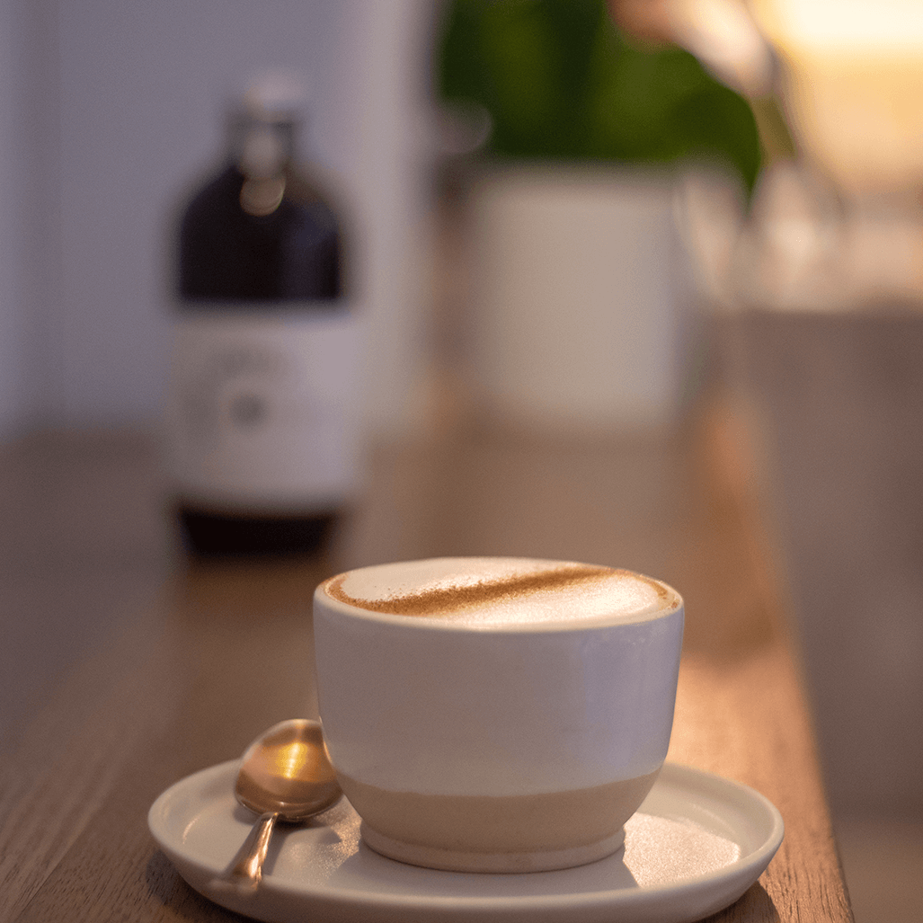 a cup of chai latte served on a white ceramic cup and a bottle of chai addict in the backgroud