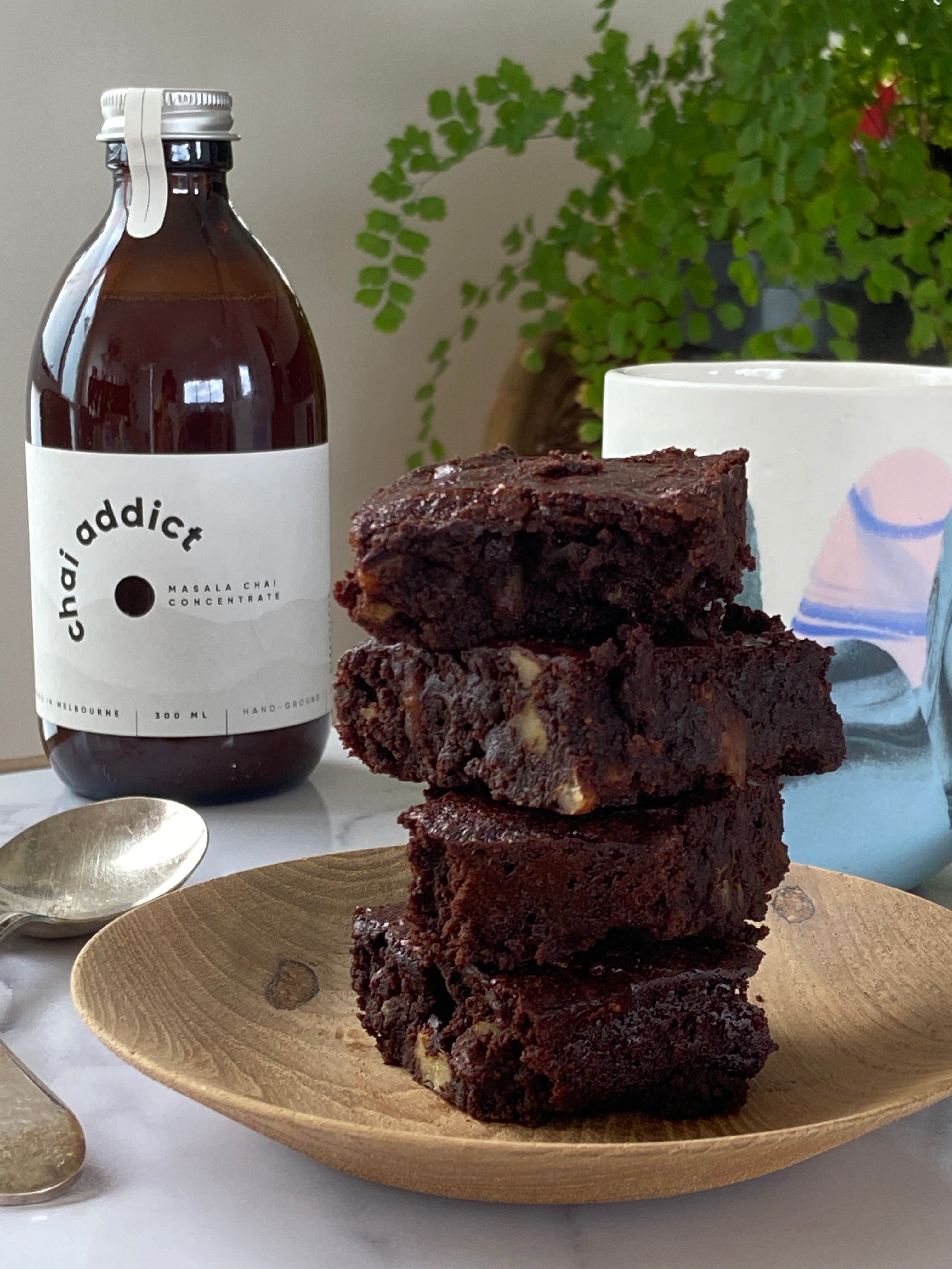 stacked slices of soft fudgey chocolate chai brownie, a bottle of chai addict and cup of chai latte