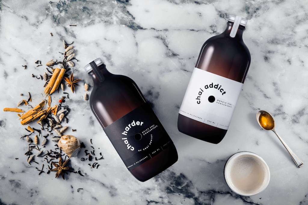 chai spices on a marble bench top next to bottle of chai harder and chai addict liquid chai tea concentrate