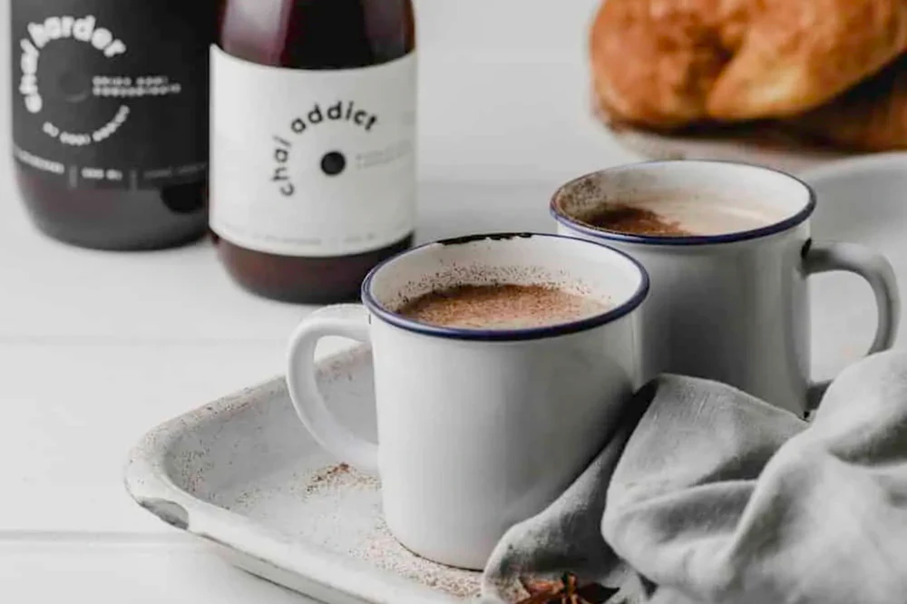 Steaming cup of aromatic chai latte served in a ceramic mug, garnished with cinnamon sticks and star anise, resting on a rustic white metal tray